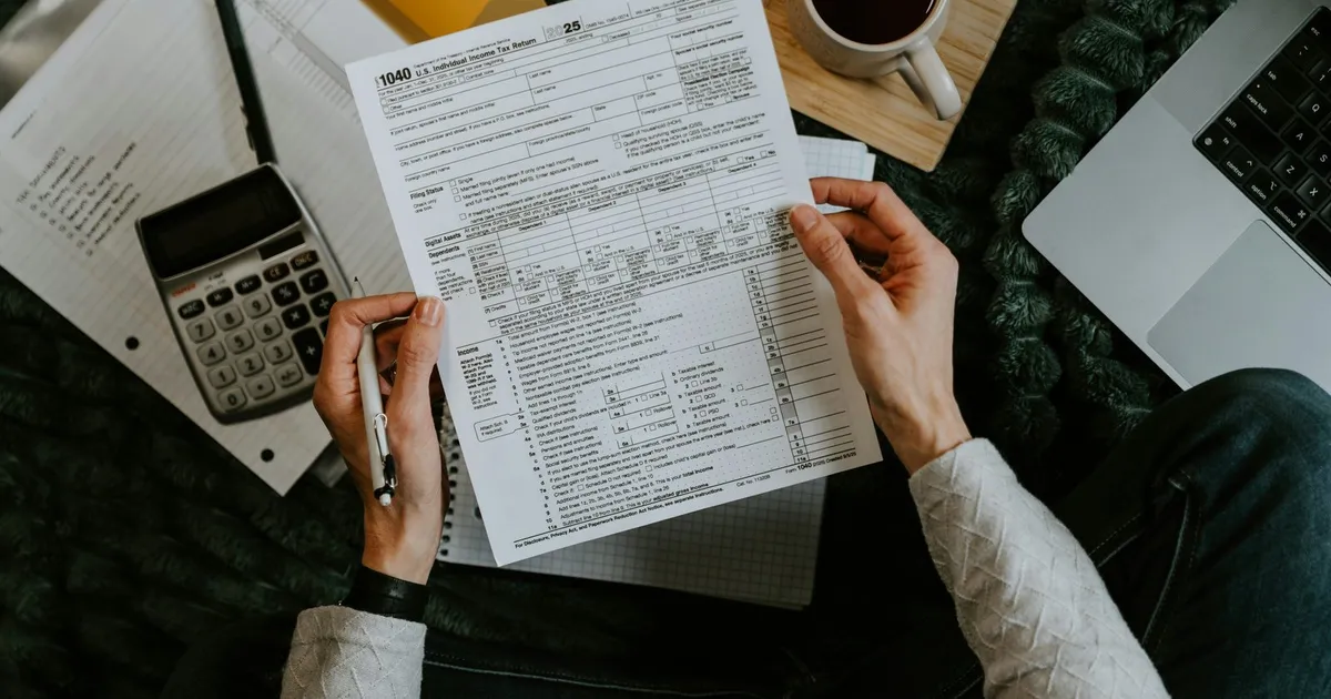 Persona revisando una factura en papel con bolígrafo, junto a una calculadora, un portátil y una taza de café.