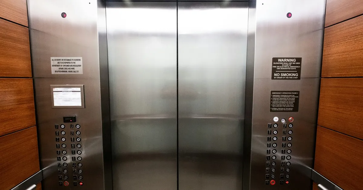 Puertas de acero de un ascensor con botoneras a ambos lados, en un portal revestido de madera.