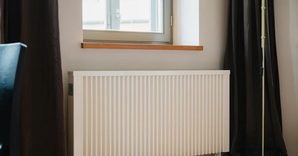 Radiador blanco bajo una ventana en una vivienda, como los que calienta una caldera central de comunidad.